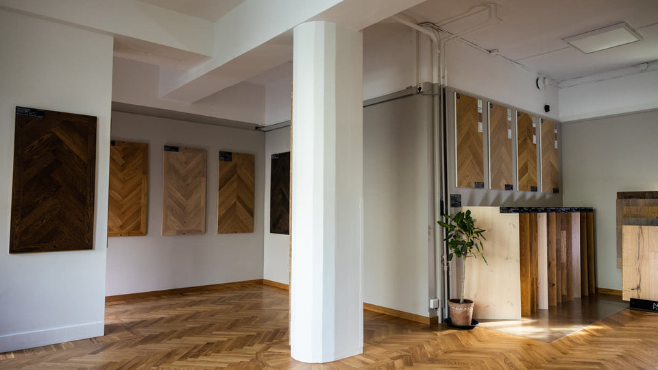 Bred interiörvy med kolonner, väggprover och stående paneler i showroom.