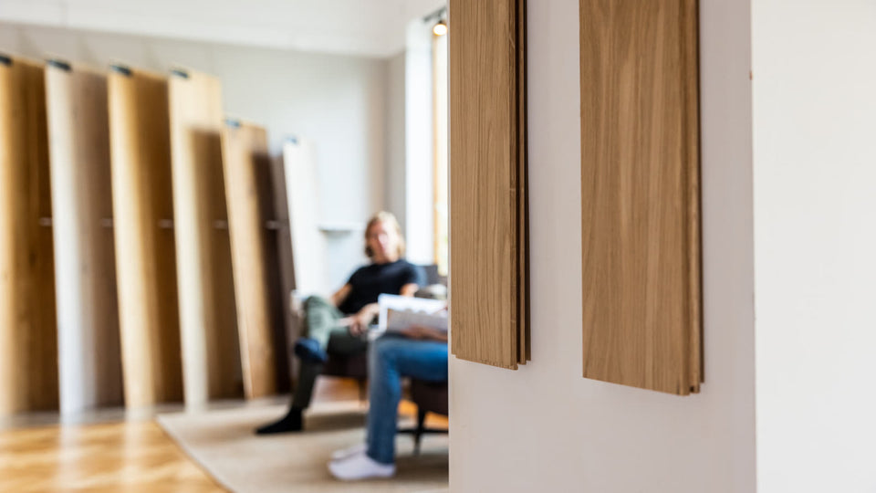 Fokus på två vertikala träprover med sittdel av showroom suddig i bakgrunden.